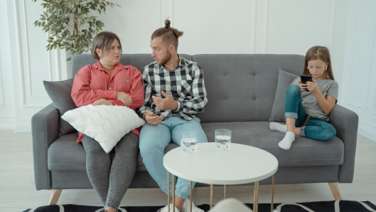 Niño sentado solo con sus padres discutiendo de fondo