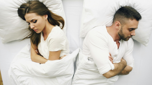 Pareja durmiendo en un dormitorio, uno roncando, el otro despierto.