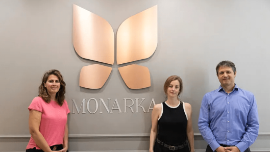 Los tres fundadores de Monarka Clinic posando frente al logotipo y el nombre “MONARKA” en la pared interior de la clínica.